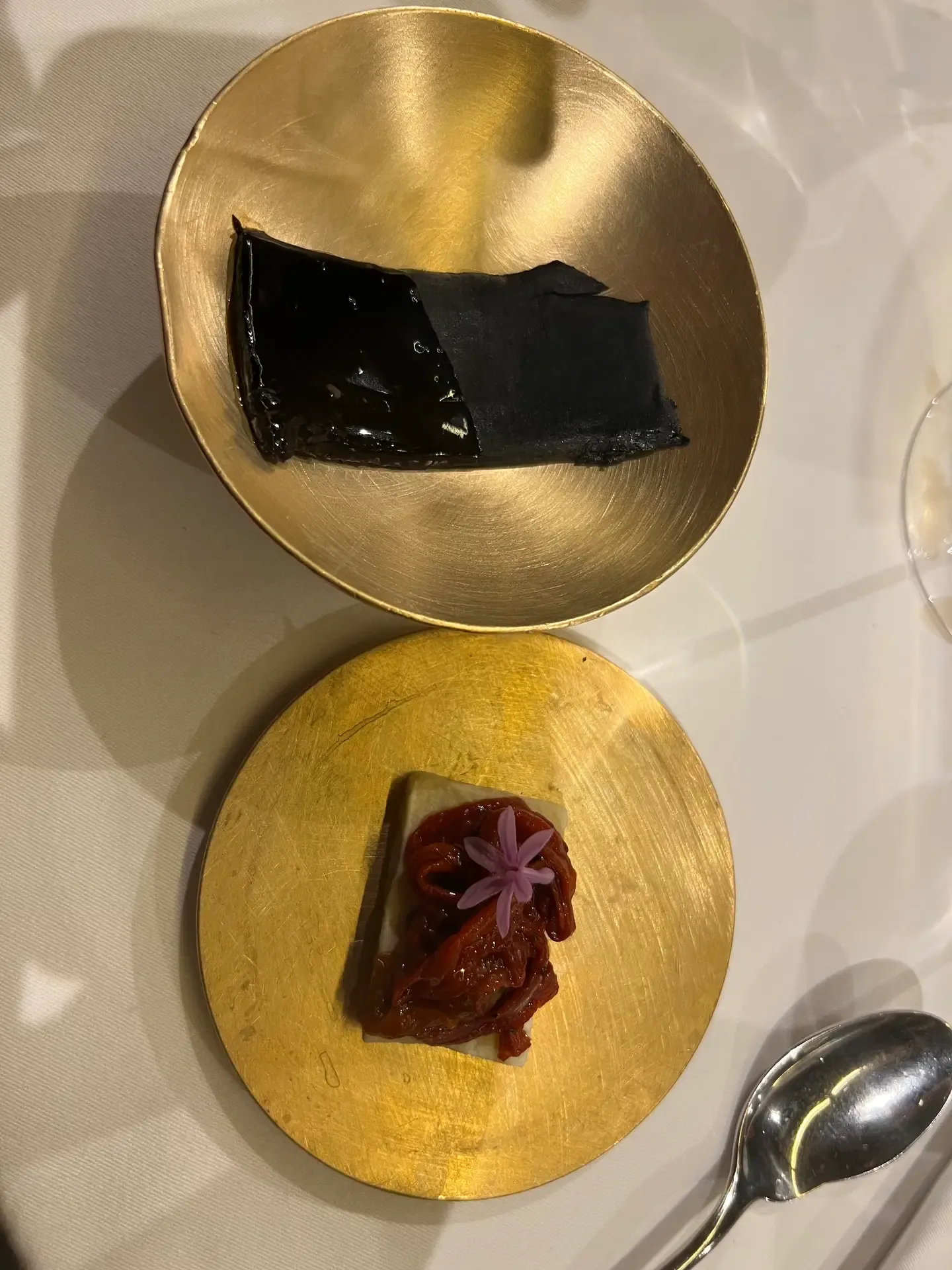A glossy black bite paired with a red fruit tartlet on gold plates at Mugaritz