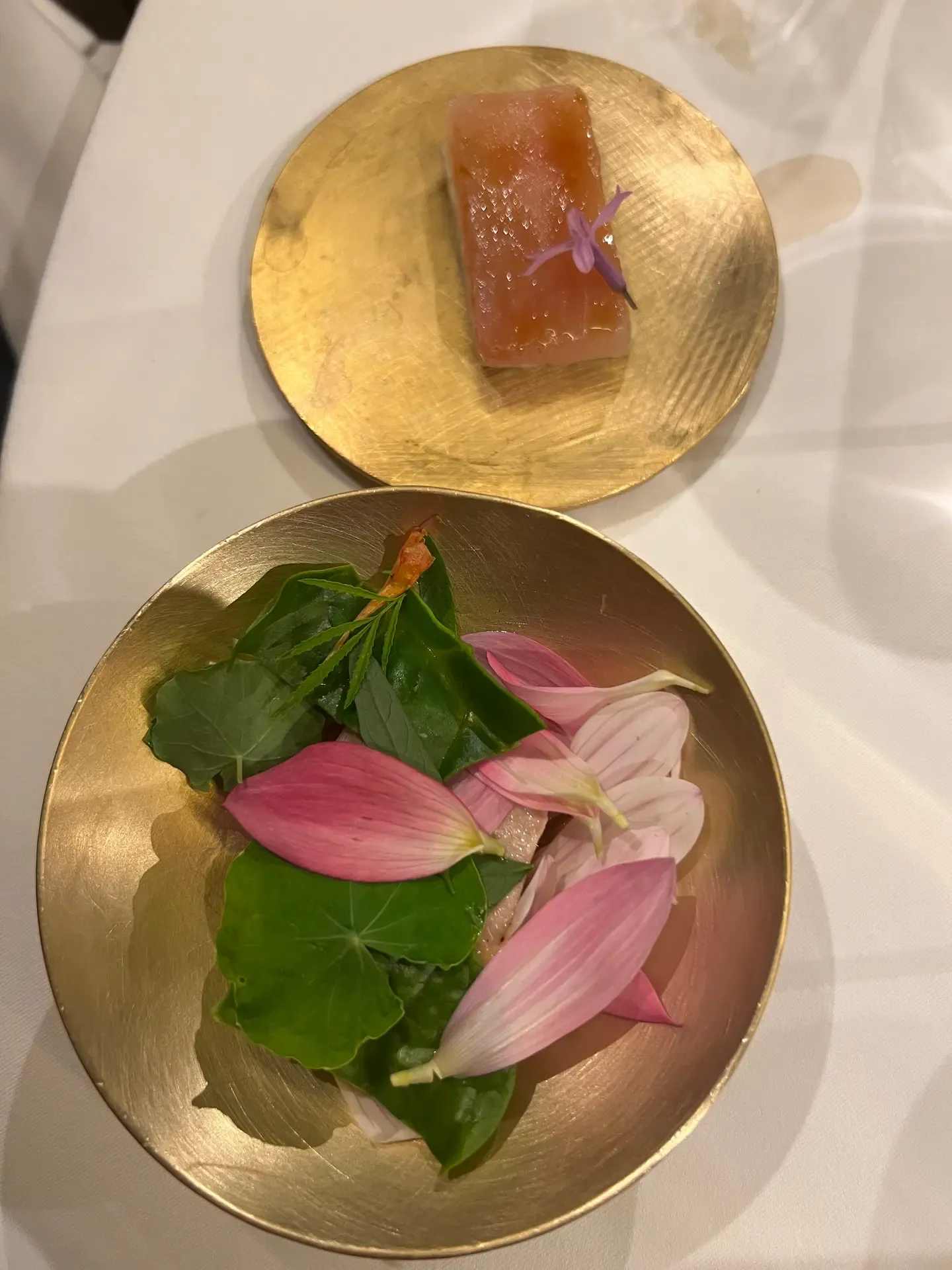 A translucent pink course with leaves and petals on a gold plate at Mugaritz